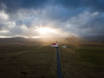 A church with a red roof and steeple sticks out against the sprawling landscape as the sun pokes through the hazy clouds.