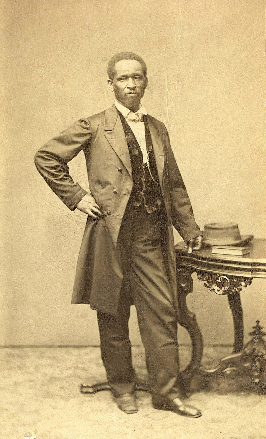 a man in a suit standing next to a table poses for a portait